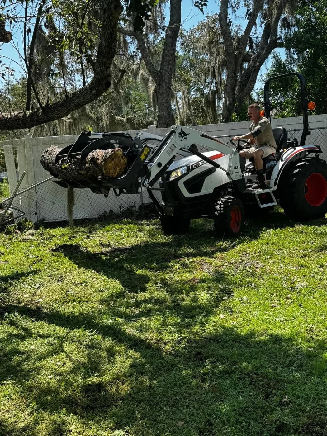 Eco Green operator running a compact loader to clear a log from a Land O' Lakes yard